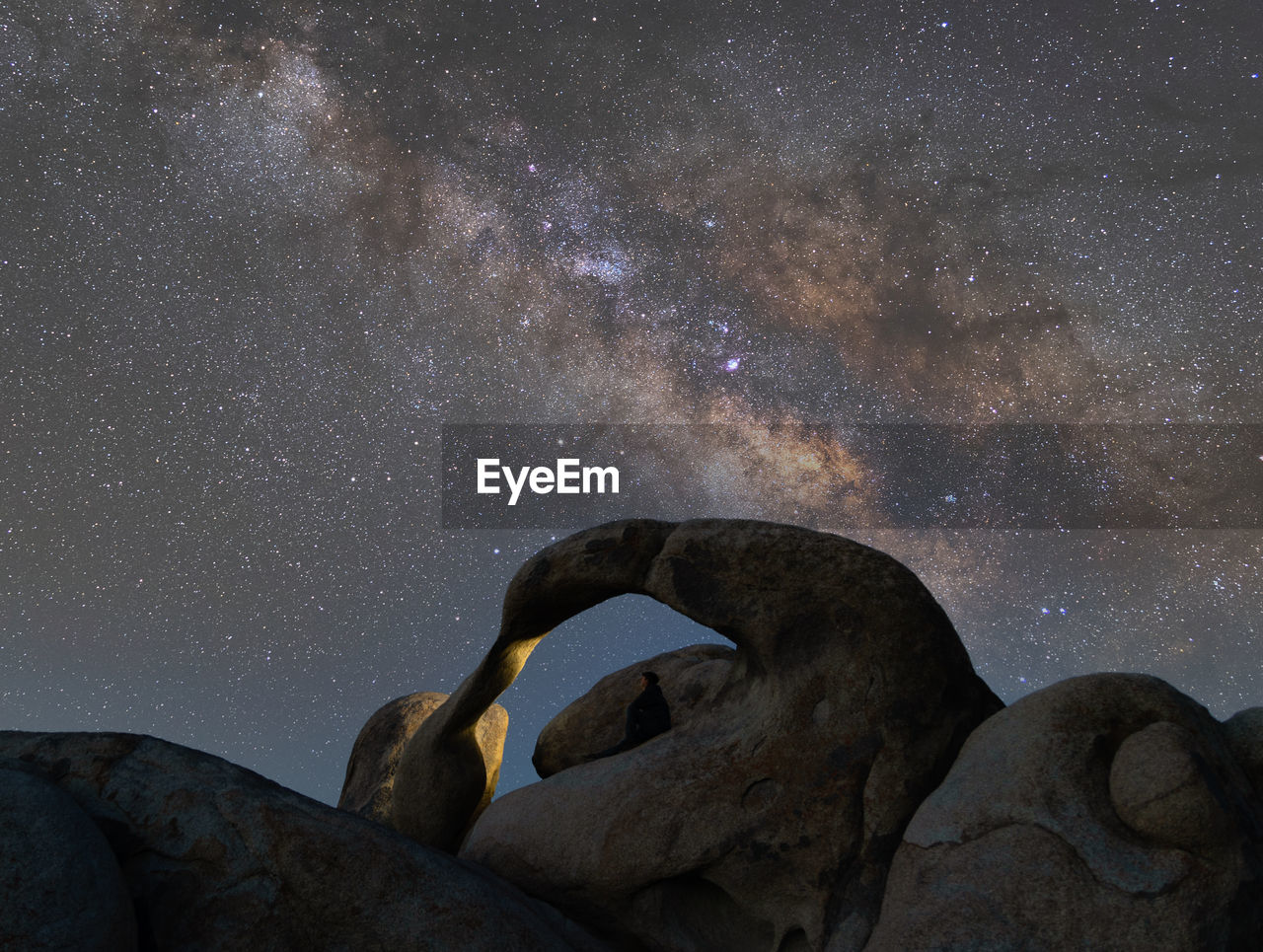 Milky way over mobius arch with a lone man sitting in the arch