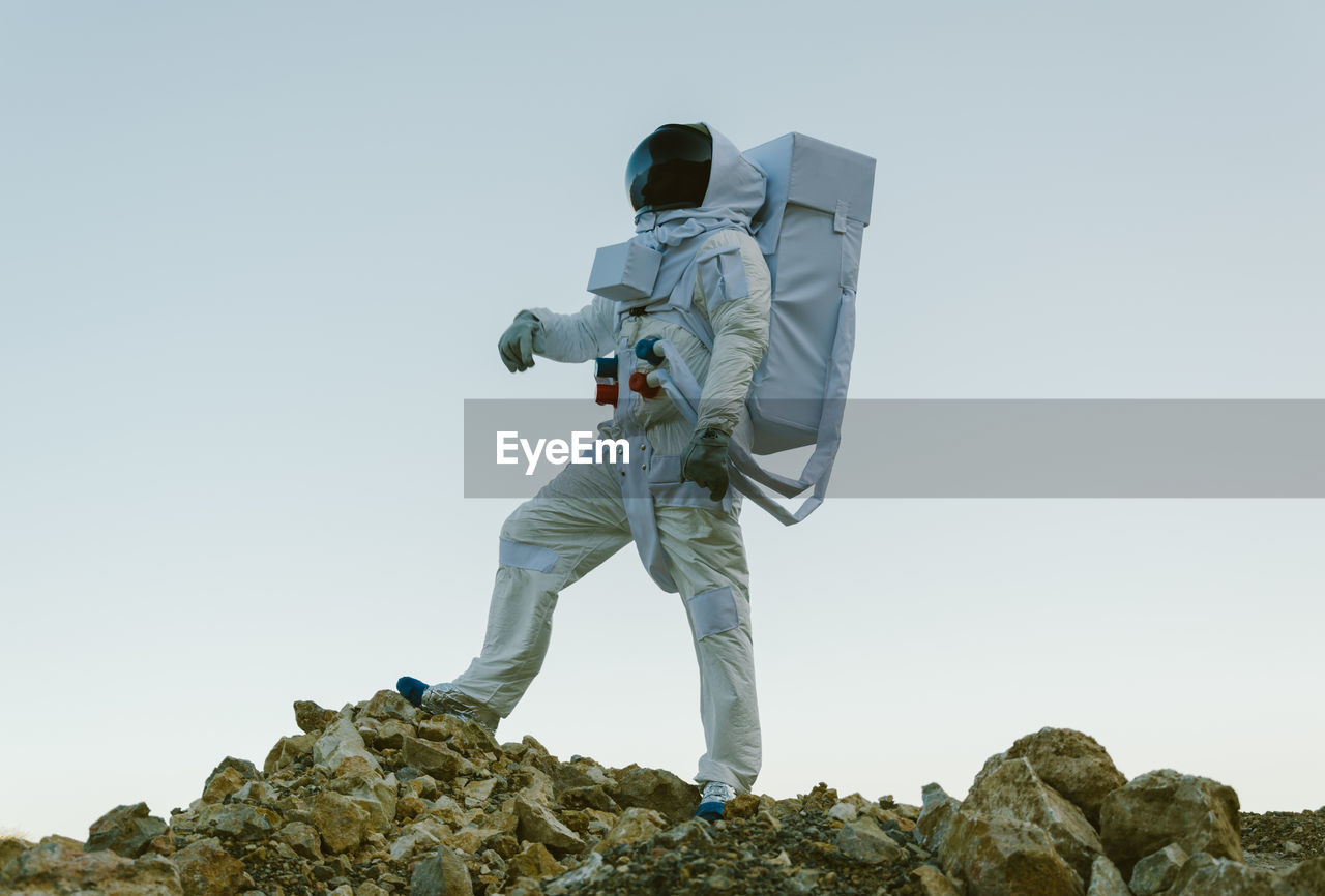 Low angle view of an astronaut standing on rock against clear sky