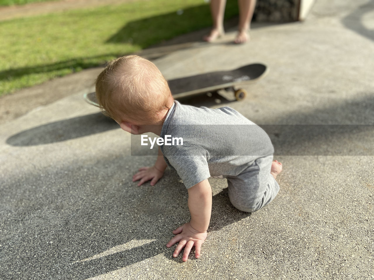 Blonde child, baby in a gray outfit crawling next to a skateboard