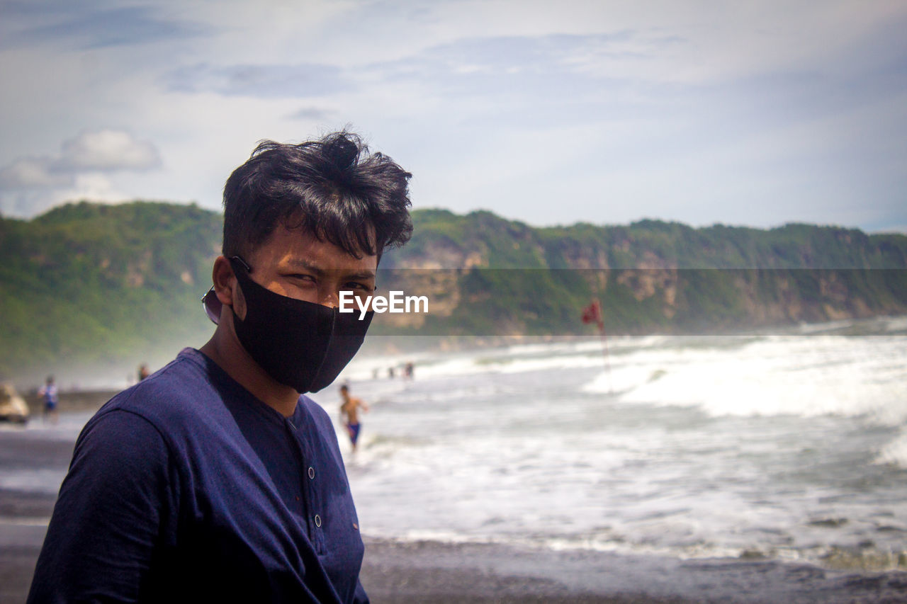 Portrait of a man standing on the beach, wearing a mask