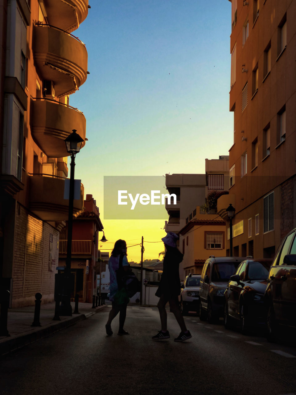 PEOPLE WALKING ON STREET AMIDST BUILDINGS IN CITY AGAINST SKY