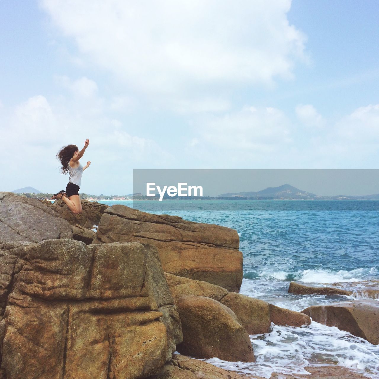 Woman jumping on rock formation on coast