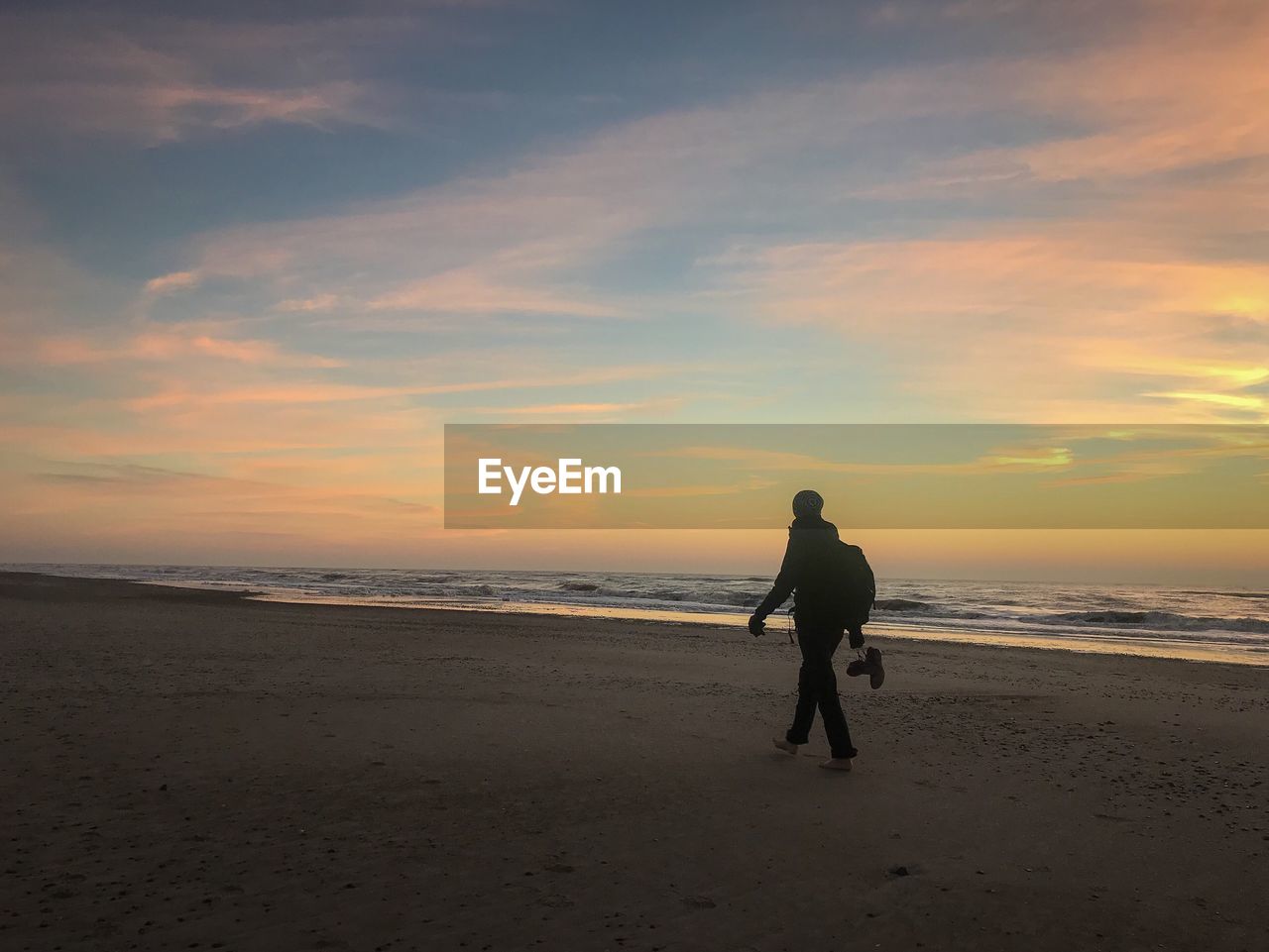 Rear view of woman on beach against sky during sunset