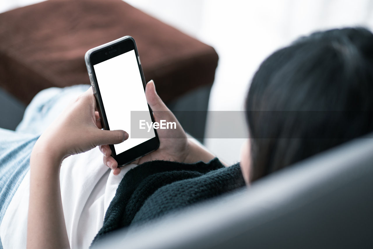 Woman using blank phone while sitting on sofa at home