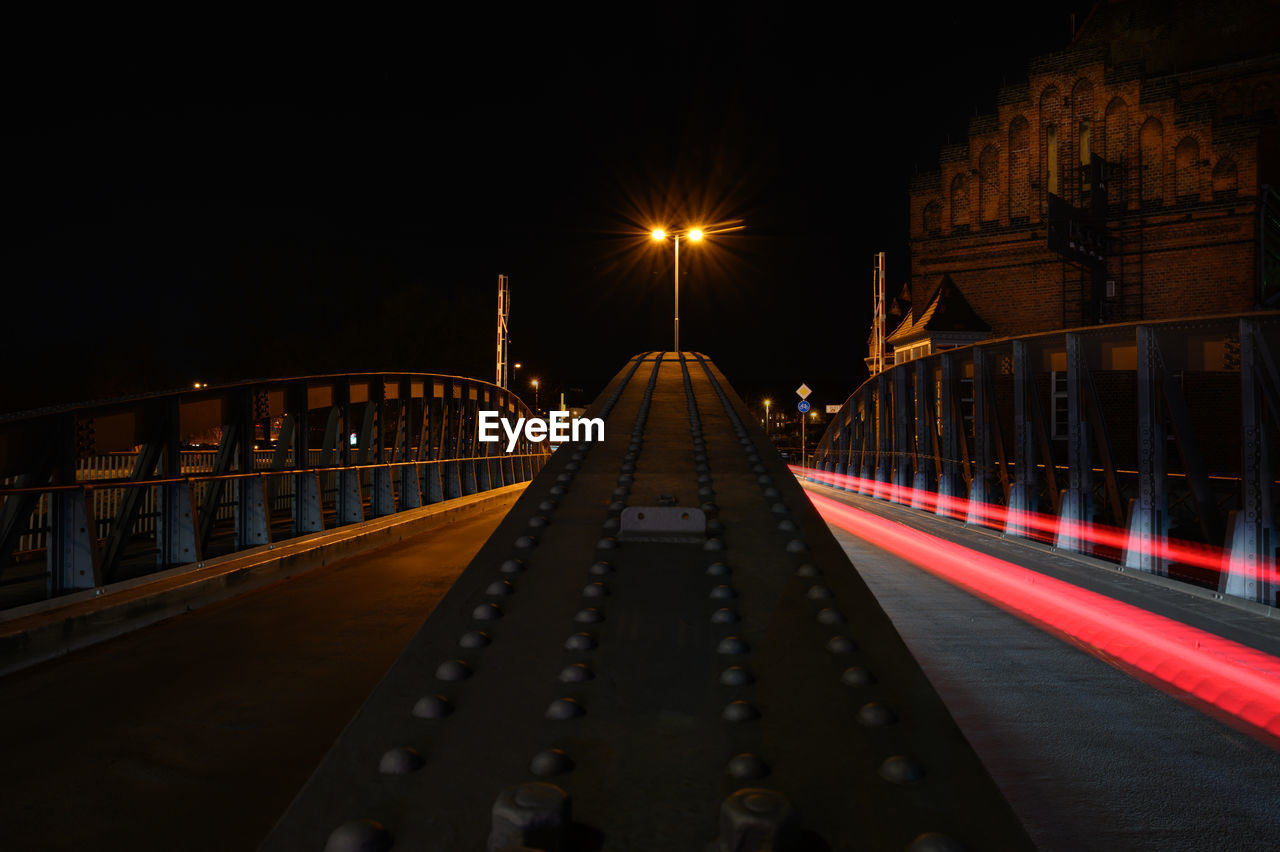 SURFACE LEVEL OF ILLUMINATED ROAD ALONG FOOTBRIDGE AT NIGHT