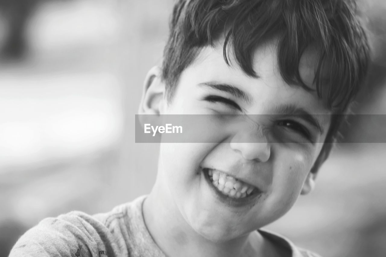 Close-up portrait of cute boy winking while smiling outdoors