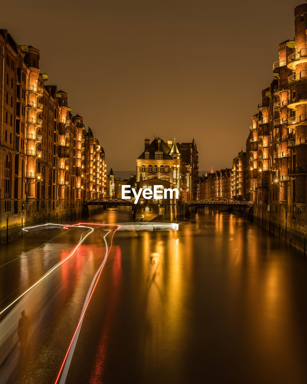 ILLUMINATED CITY BUILDINGS BY ROAD AGAINST SKY AT NIGHT