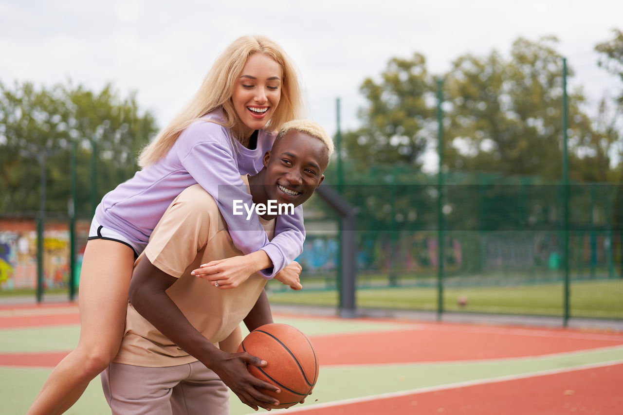 Smiling man carrying girlfriend on back at sports court