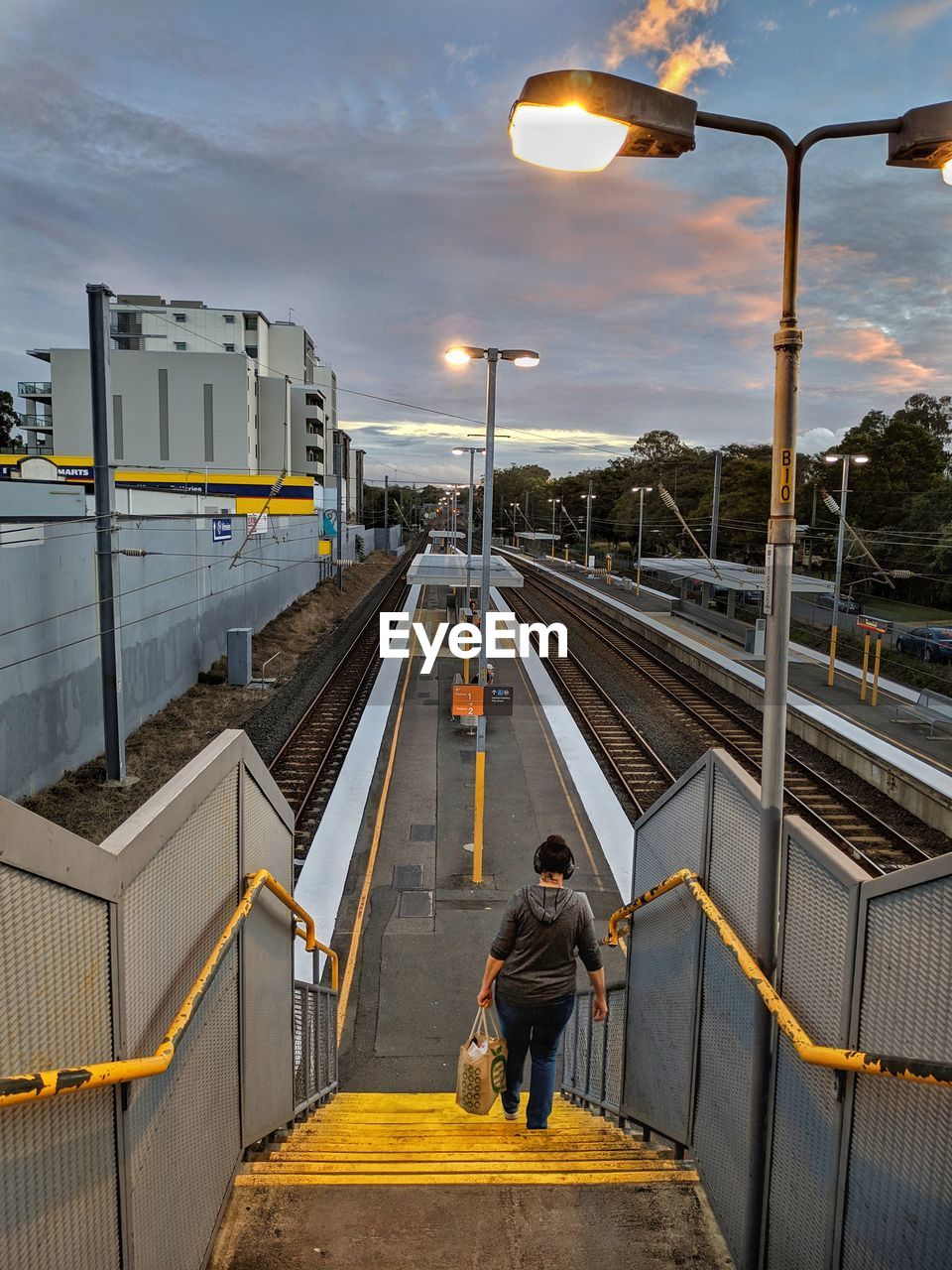 Rear view of woman moving down on staircase at railroad station platform against sky