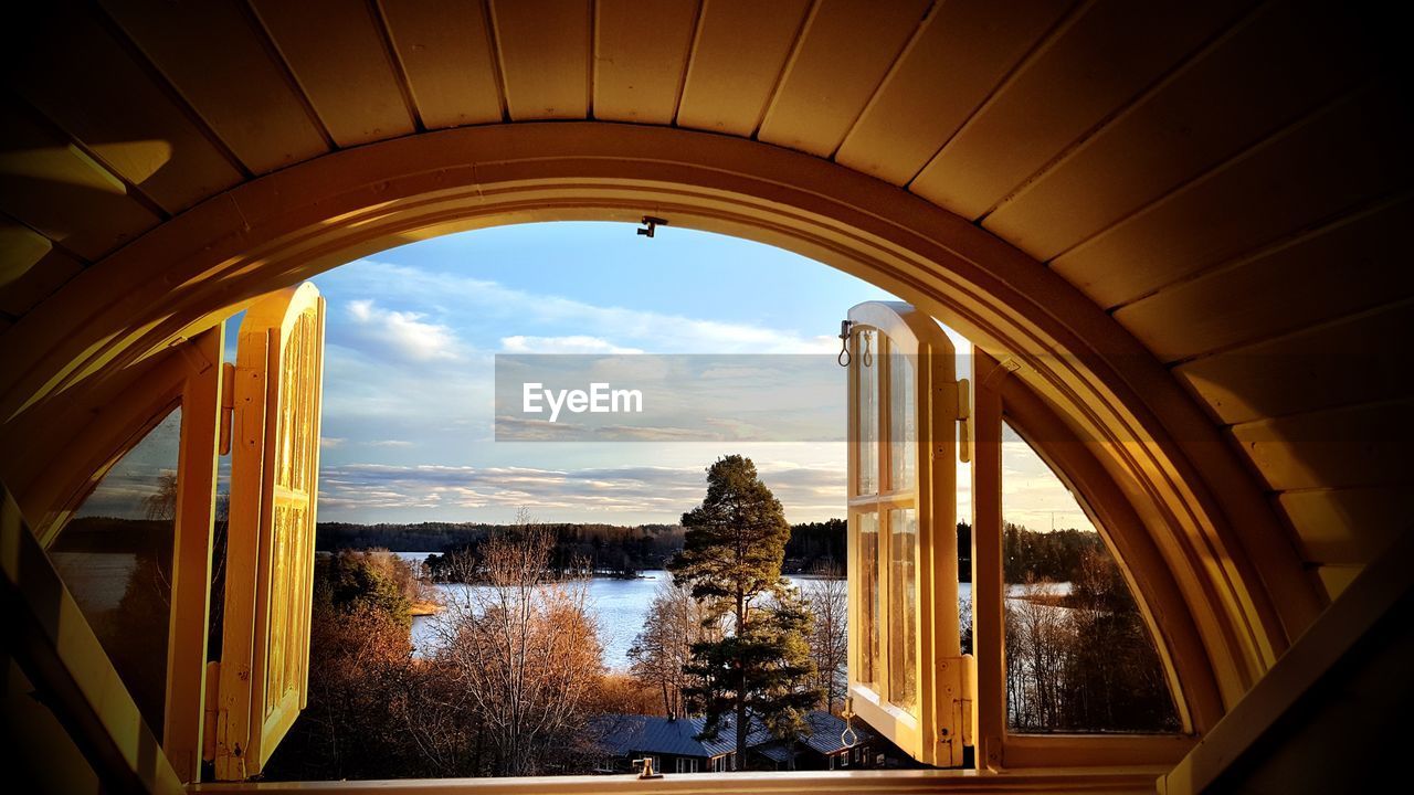 Scenic view of lake by trees seen through window at sunset