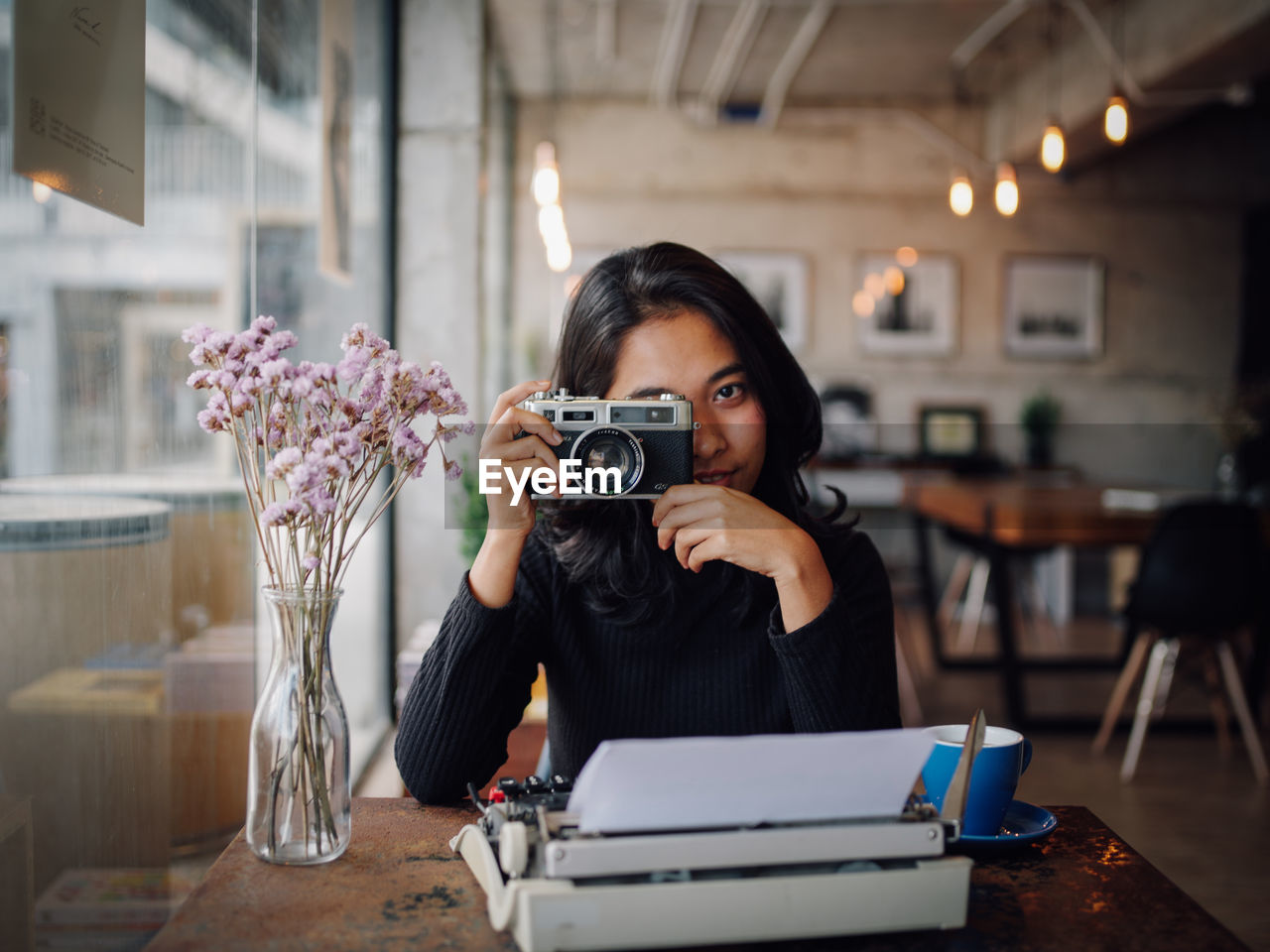 Woman photographing with camera at table in cafe