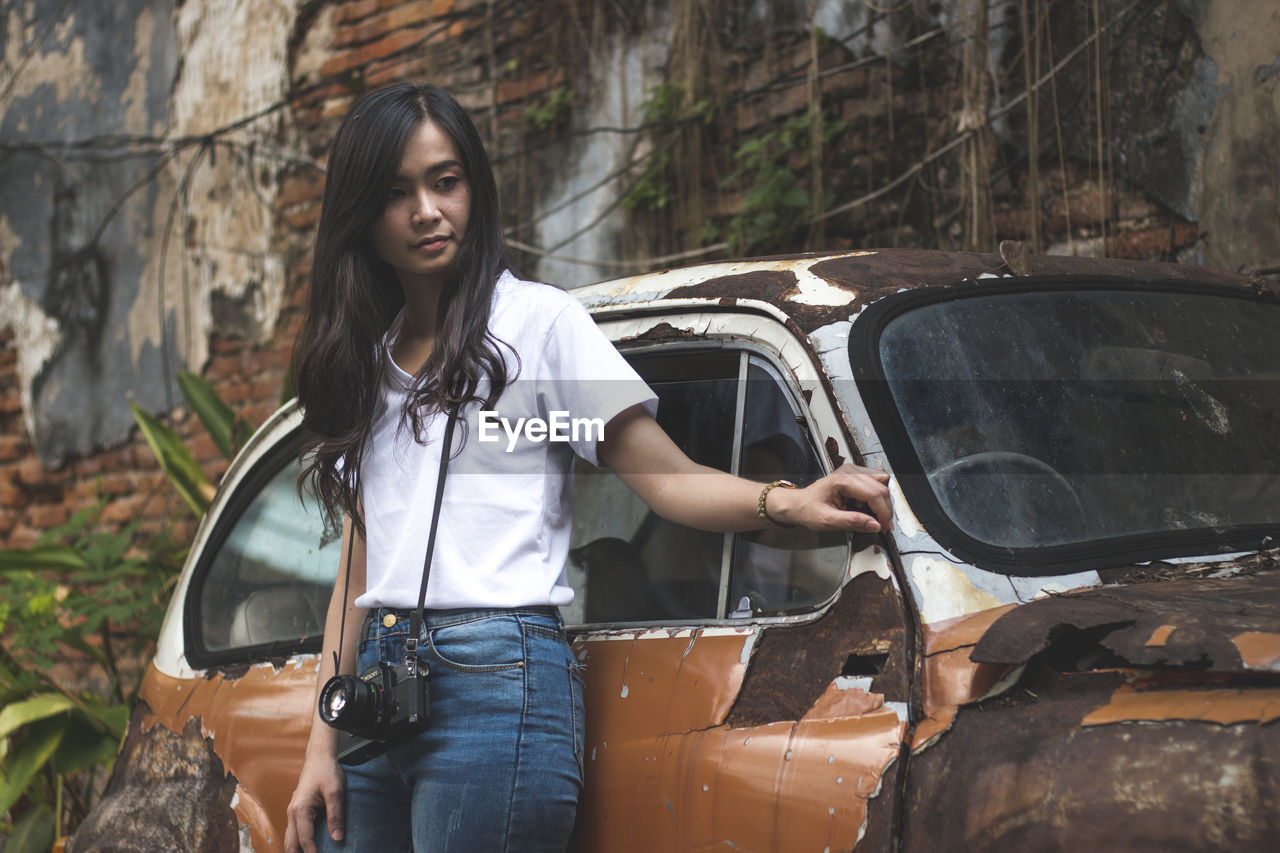 Young woman smiling while standing by abandoned car