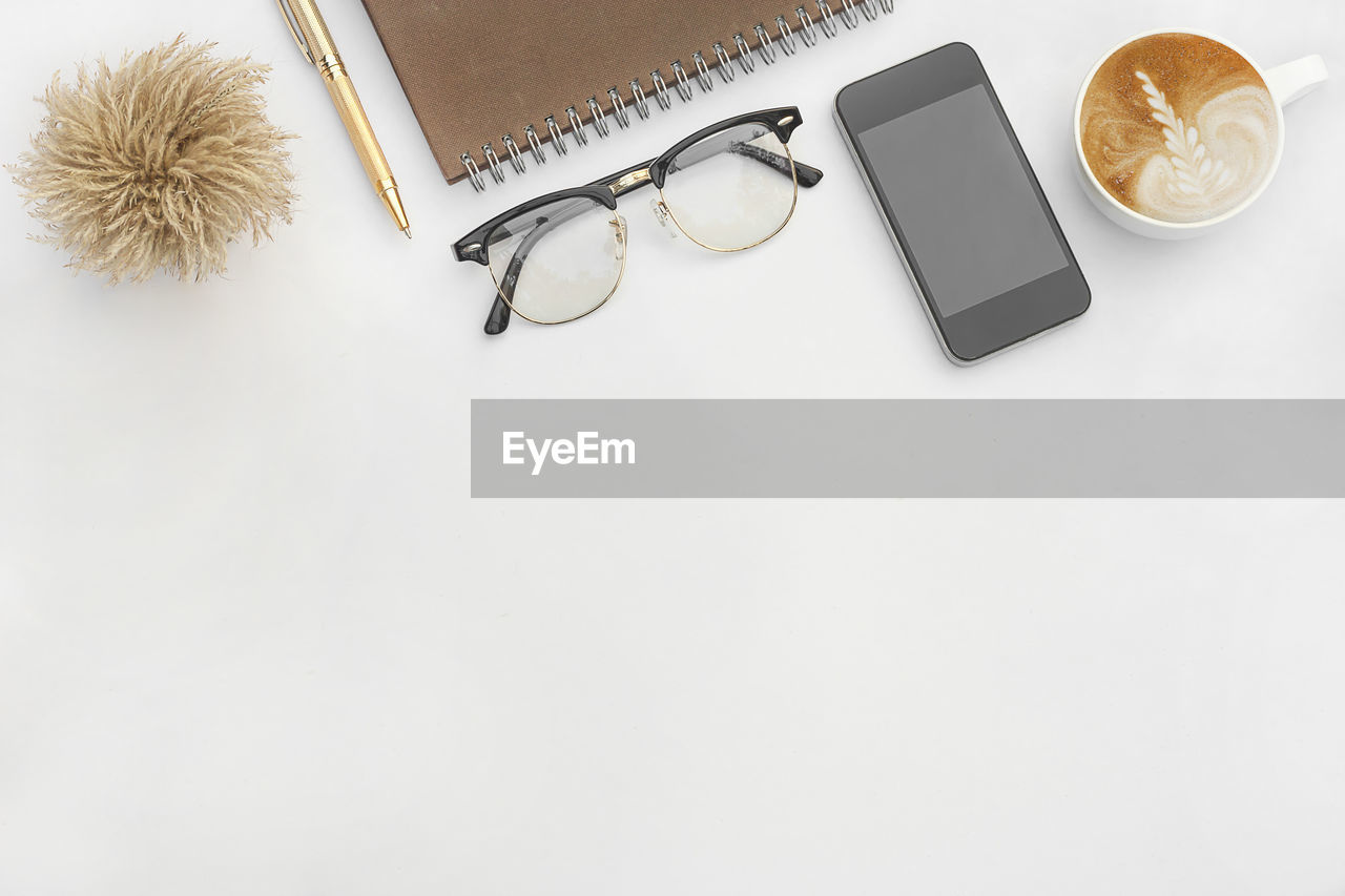 High angle view of coffee cup with mobile phone and eyeglasses on white background