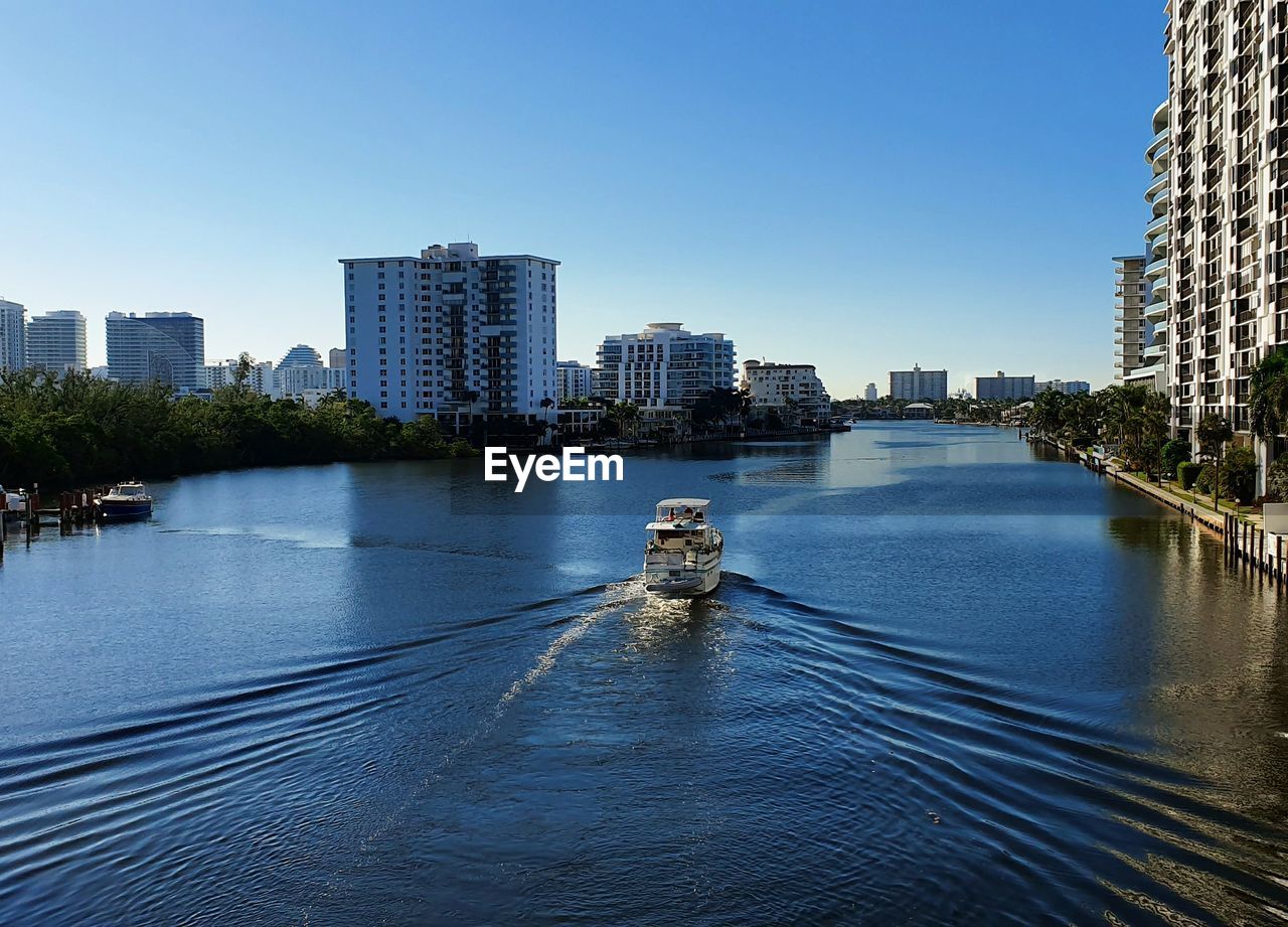 RIVER AMIDST MODERN BUILDINGS AGAINST CLEAR SKY