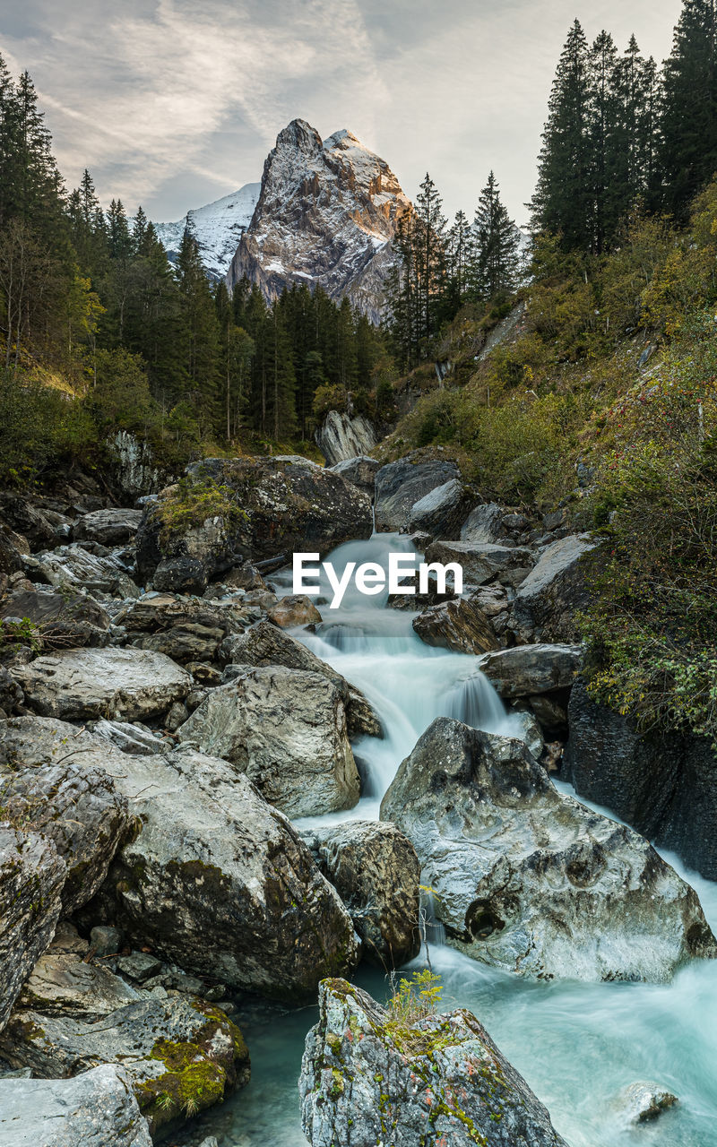 River flowing through rocks in forest against mountains and sky