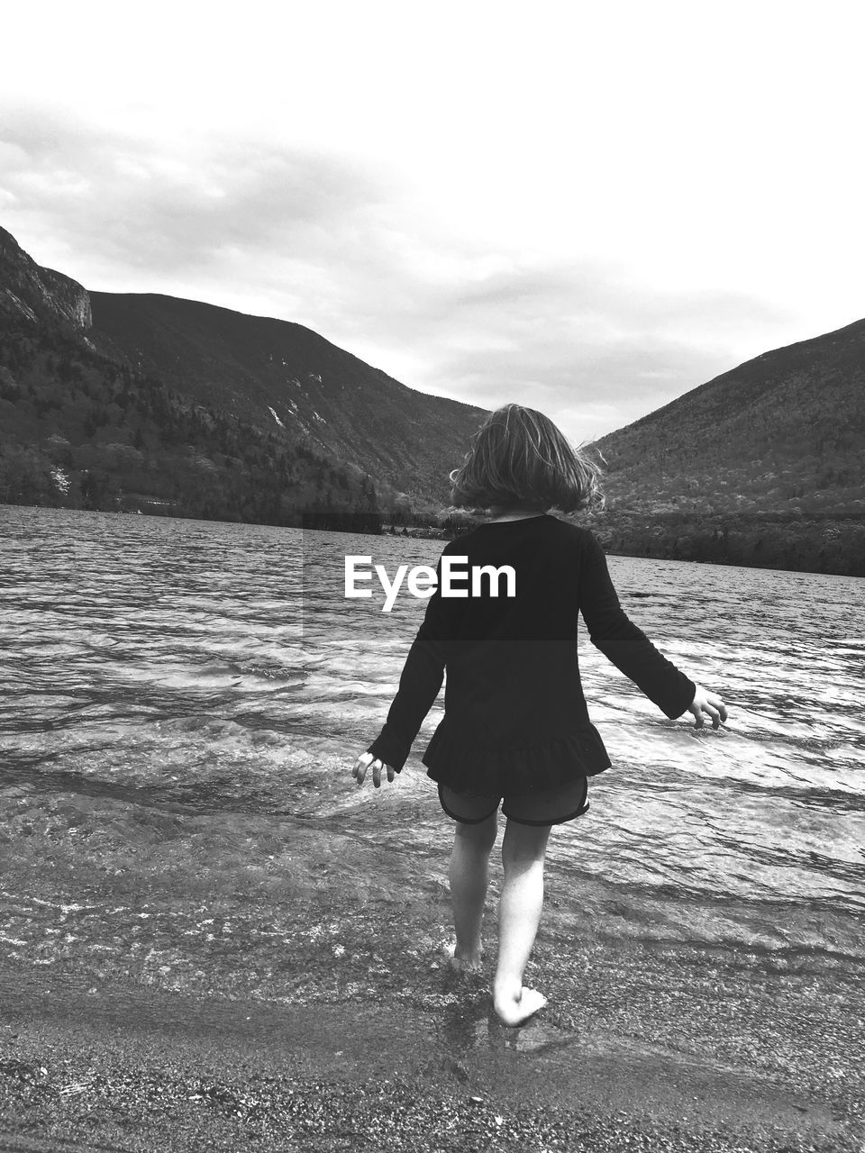 Rear view of girl standing on beach against mountain range