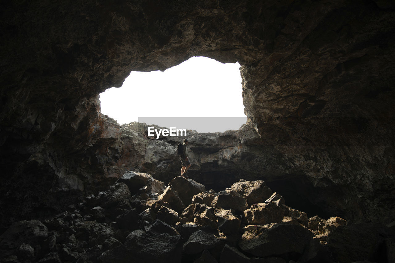 Low angle view of man standing on rock in cave against clear sky