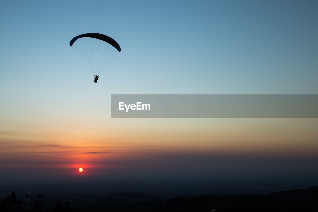 Low angle view of silhouette person paragliding against sky during sunset