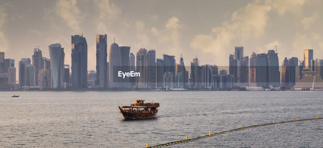 Doha skyline from the corniche promenade sunset shot showing dhow with qatar flag in the arabic gulf