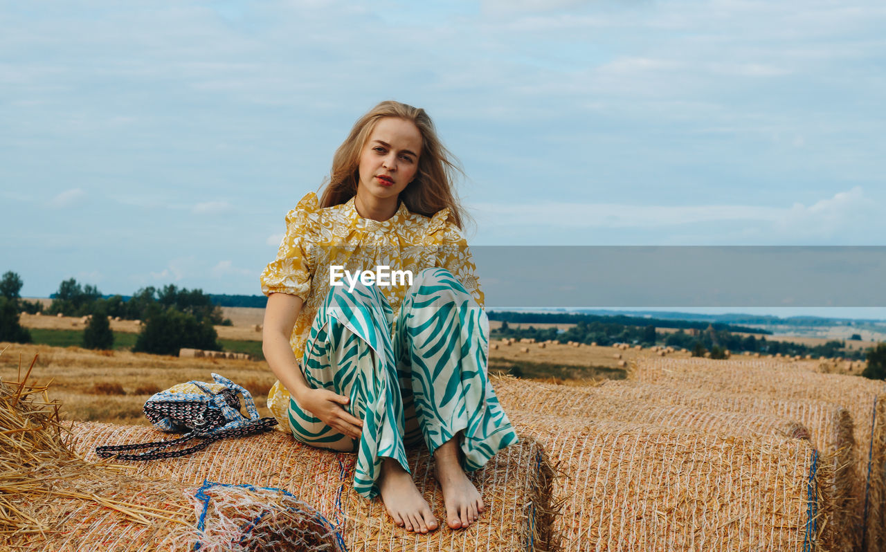 Young woman sitting on field against sky