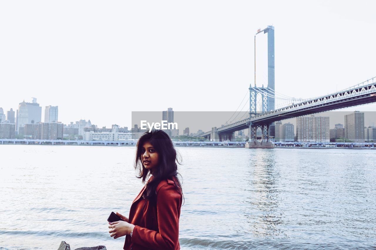 Portrait of young woman standing by east river in city