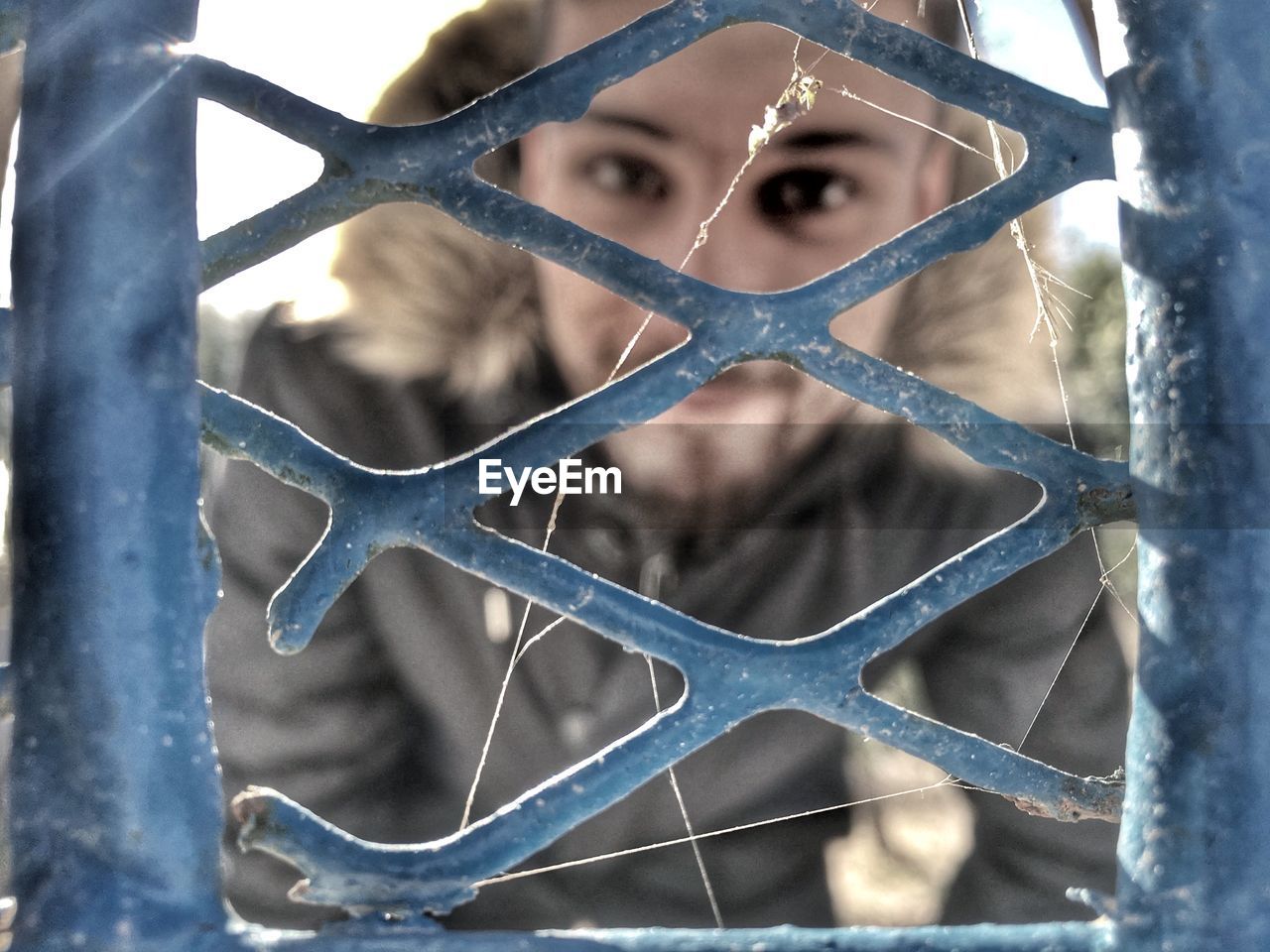 Close-up portrait of man seen through fence during winter
