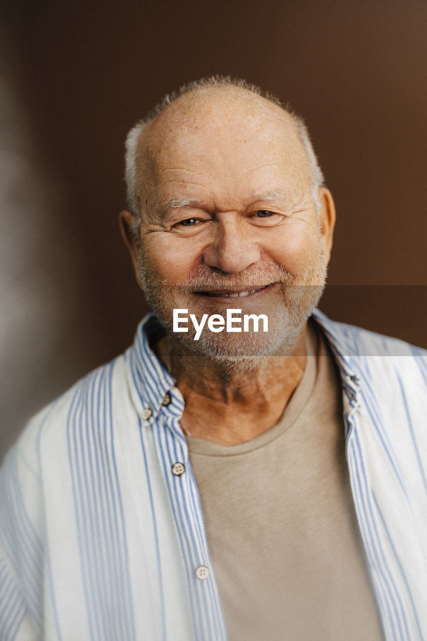 Portrait of smiling elderly man against brown background