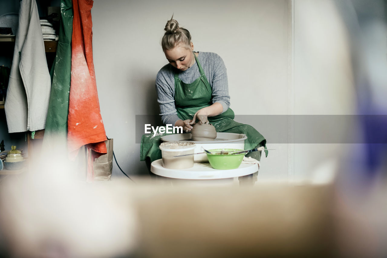 Woman potter moulding walls of clay ware on potters wheel
