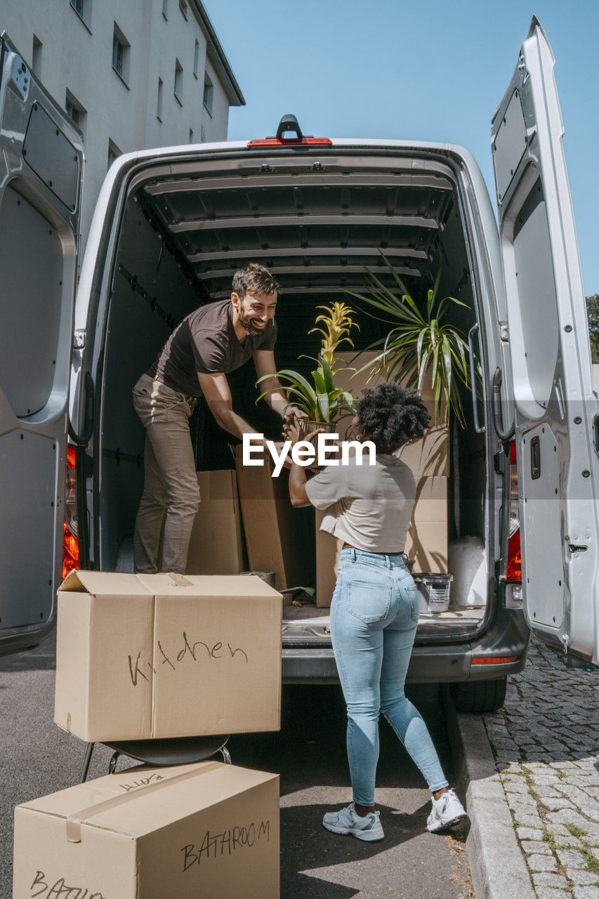 Multiracial couple helping each other while unloading plants from van trunk