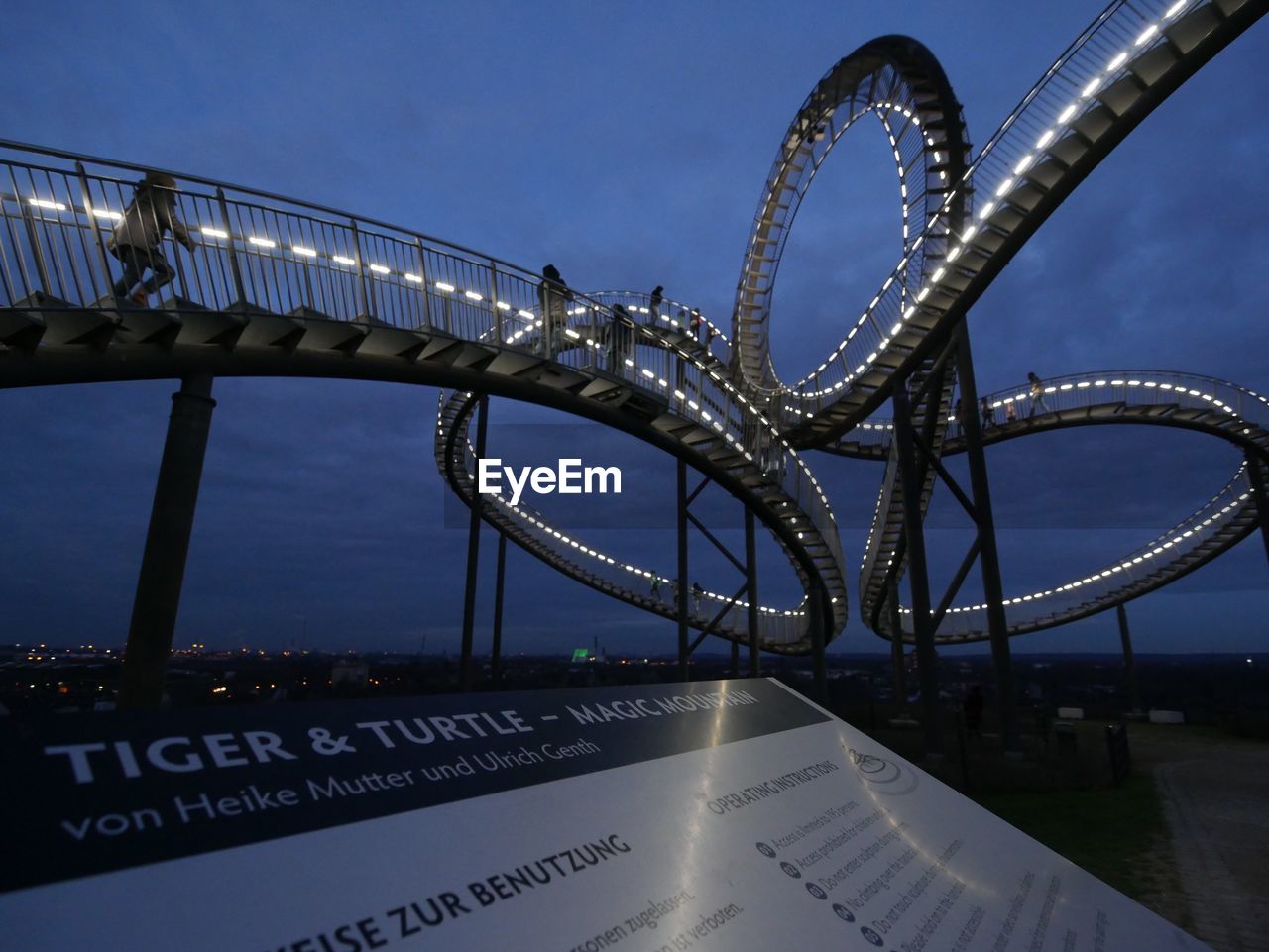 Information sign by illuminated tiger and turtle  magic mountain against sky at dusk