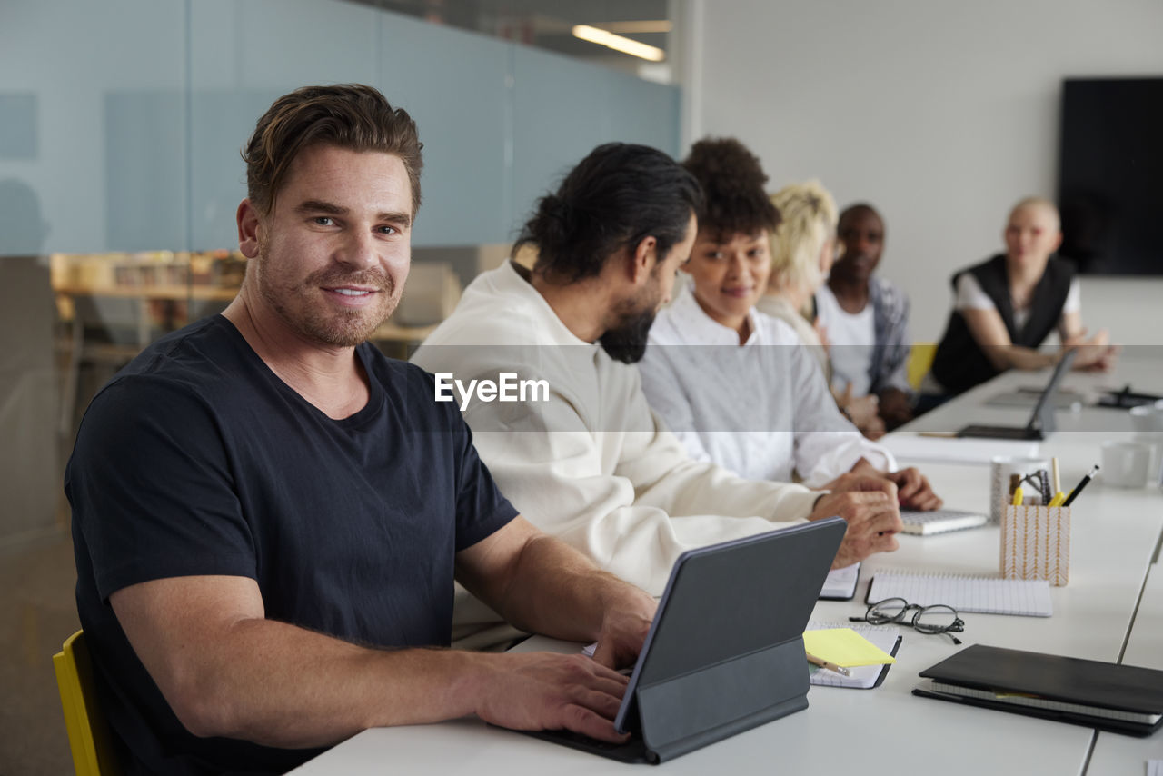 Man sitting at business meeting with digital tablet and looking at camera