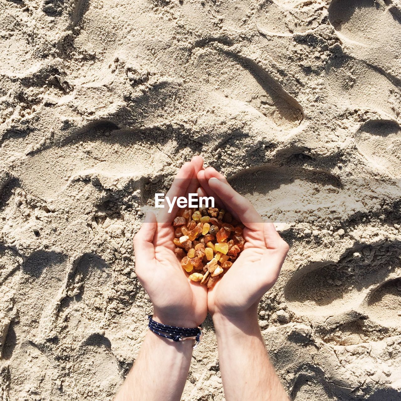 Cropped image of hands holding gravels over sand at beach