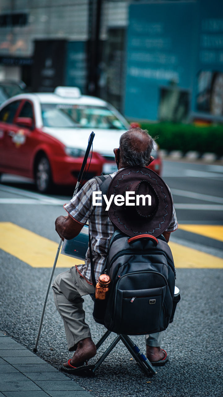 REAR VIEW OF MAN HOLDING CAR ON ROAD