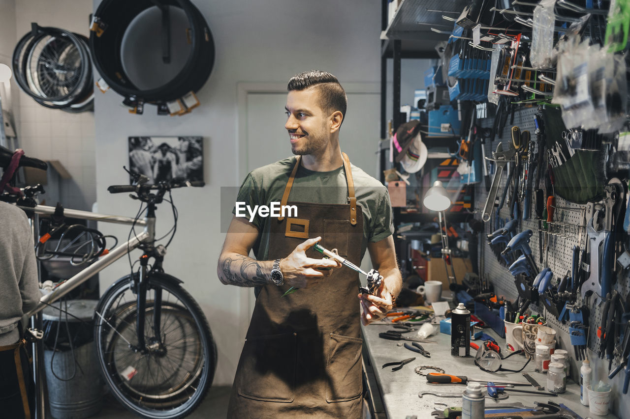 Smiling male mechanic looking at colleague while repairing pedal in workshop