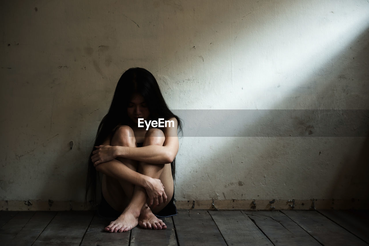 Full length of depressed woman sitting against wall