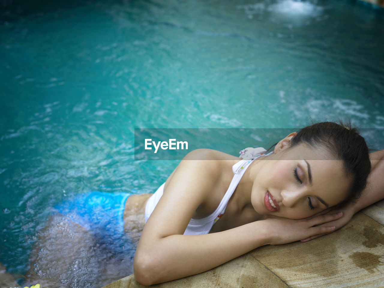 Young woman sleeping in swimming pool at tourist resort