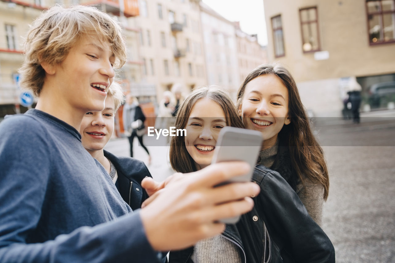 Happy male and female friends looking at mobile phone in city