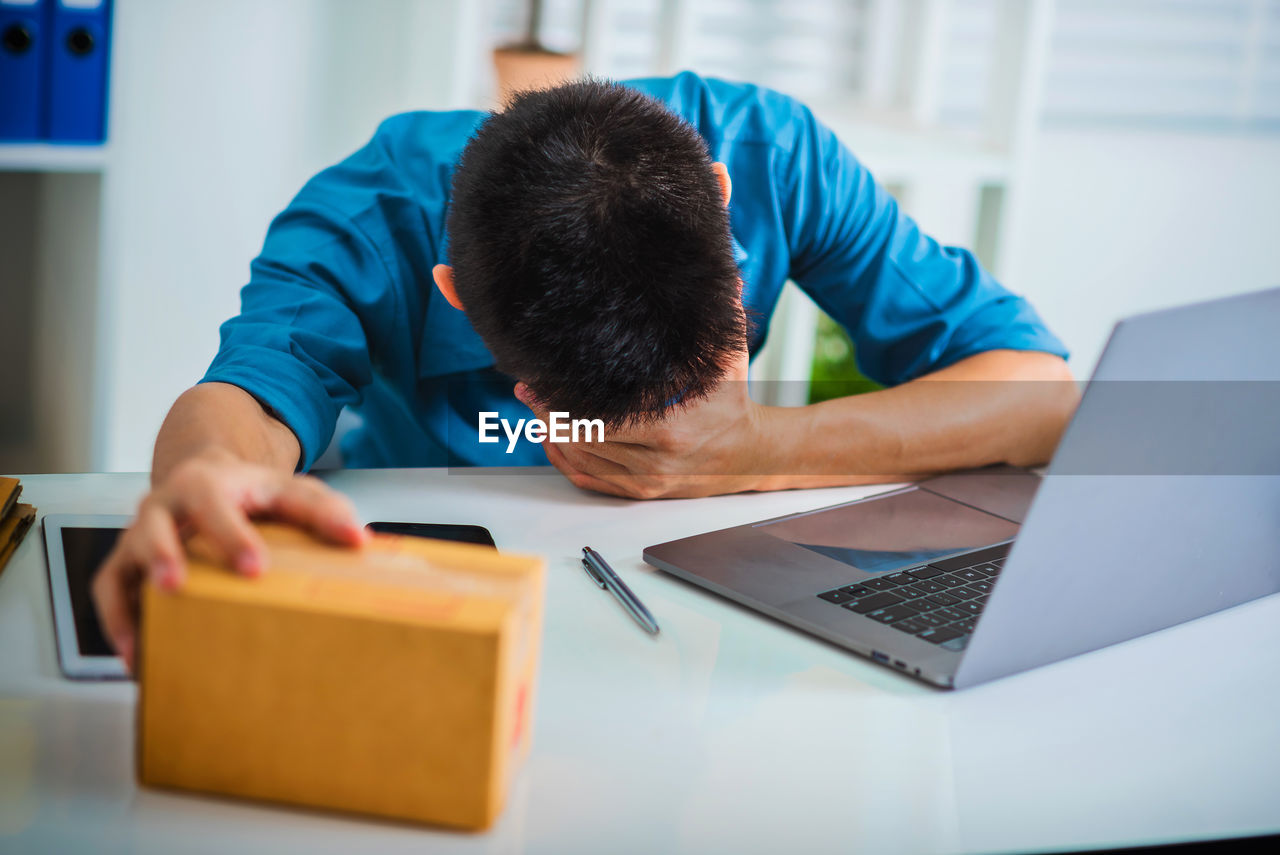 Sad man holding package by laptop on table