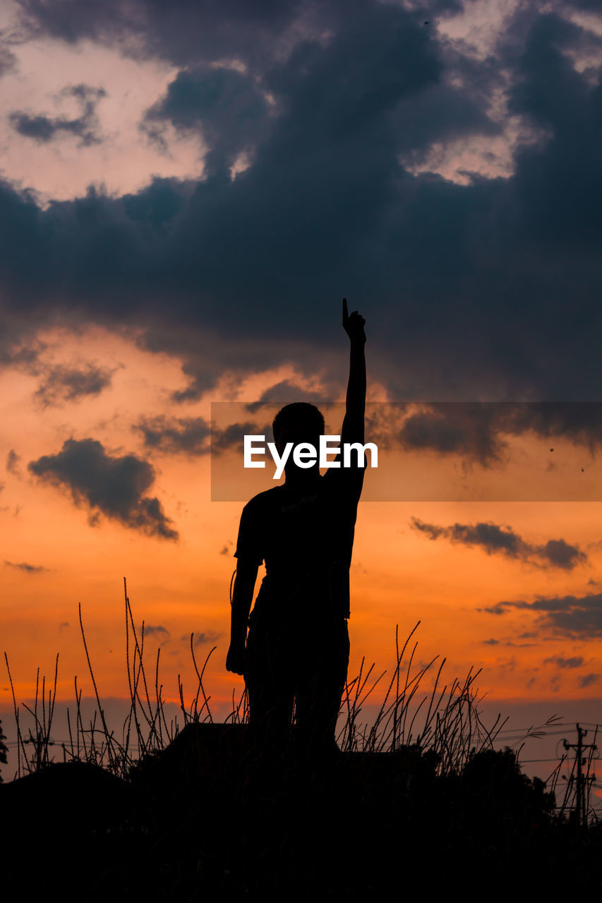 Silhouette woman with arms raised against sky during sunset