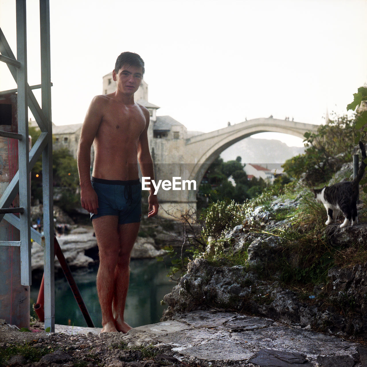 FULL LENGTH OF SHIRTLESS MAN STANDING ON BRIDGE