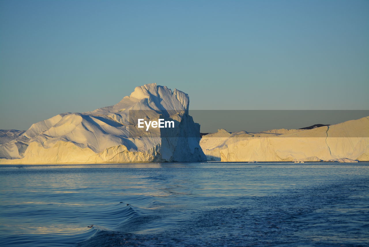 Scenic view of sea against clear sky with beautiful icebergs in the midnight sun ilulissat greenland