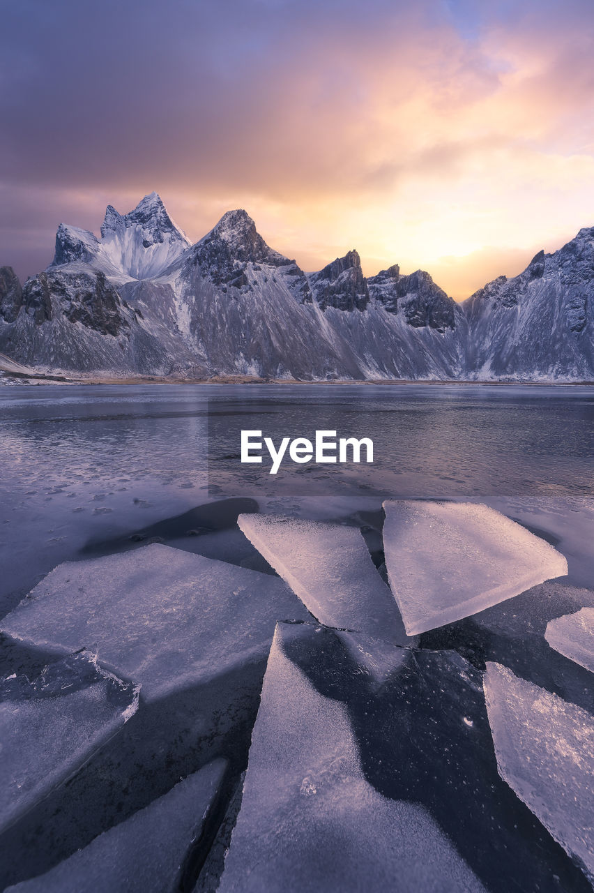 Scenic view of frozen beach against snowy mountains in winter evening in iceland