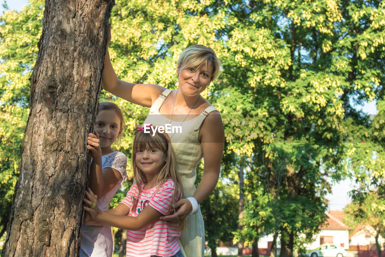 Portrait of mother with children standing against trees in park