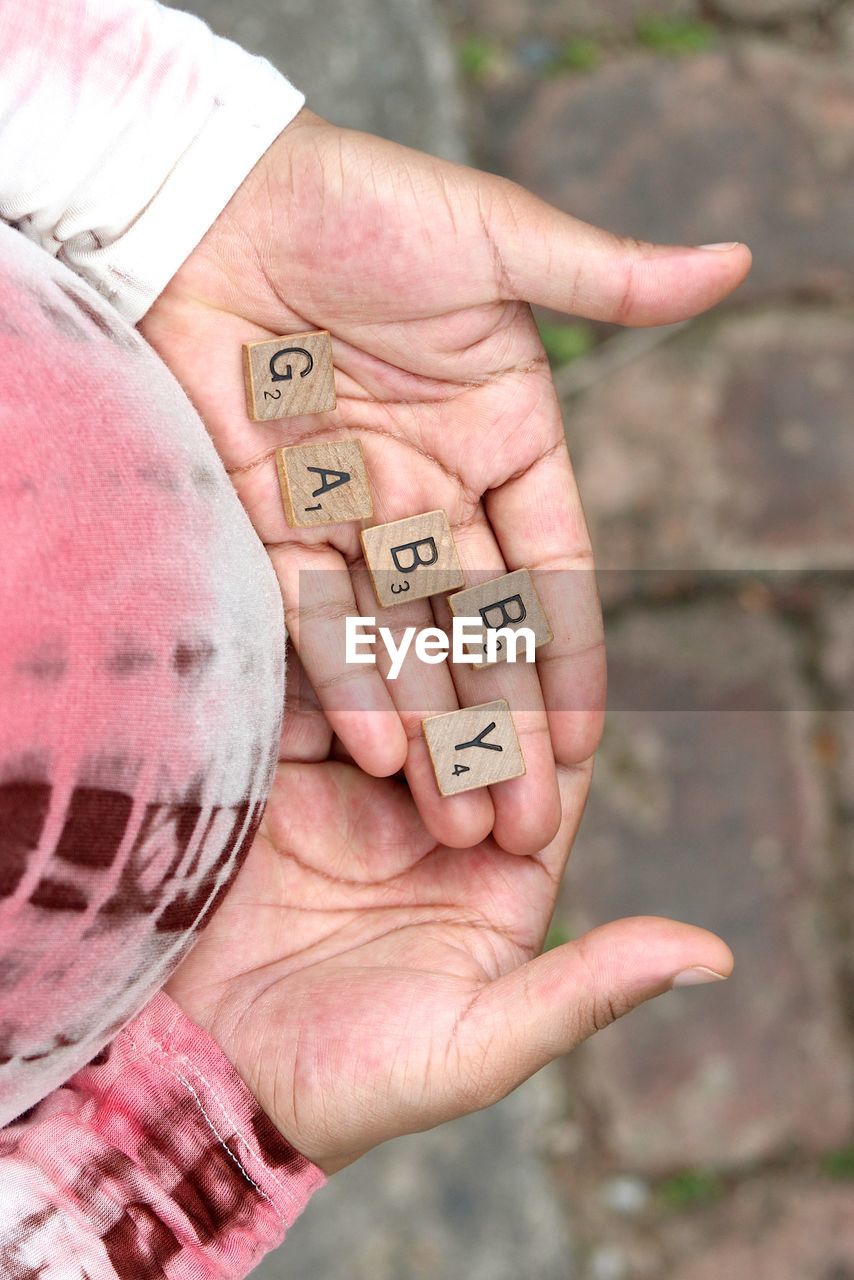 Cropped image of pregnant woman holding wooden alphabets on palm