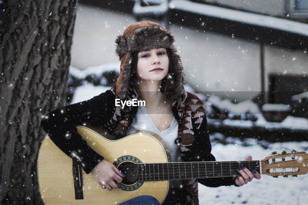 Portrait of woman playing guitar during snowfall