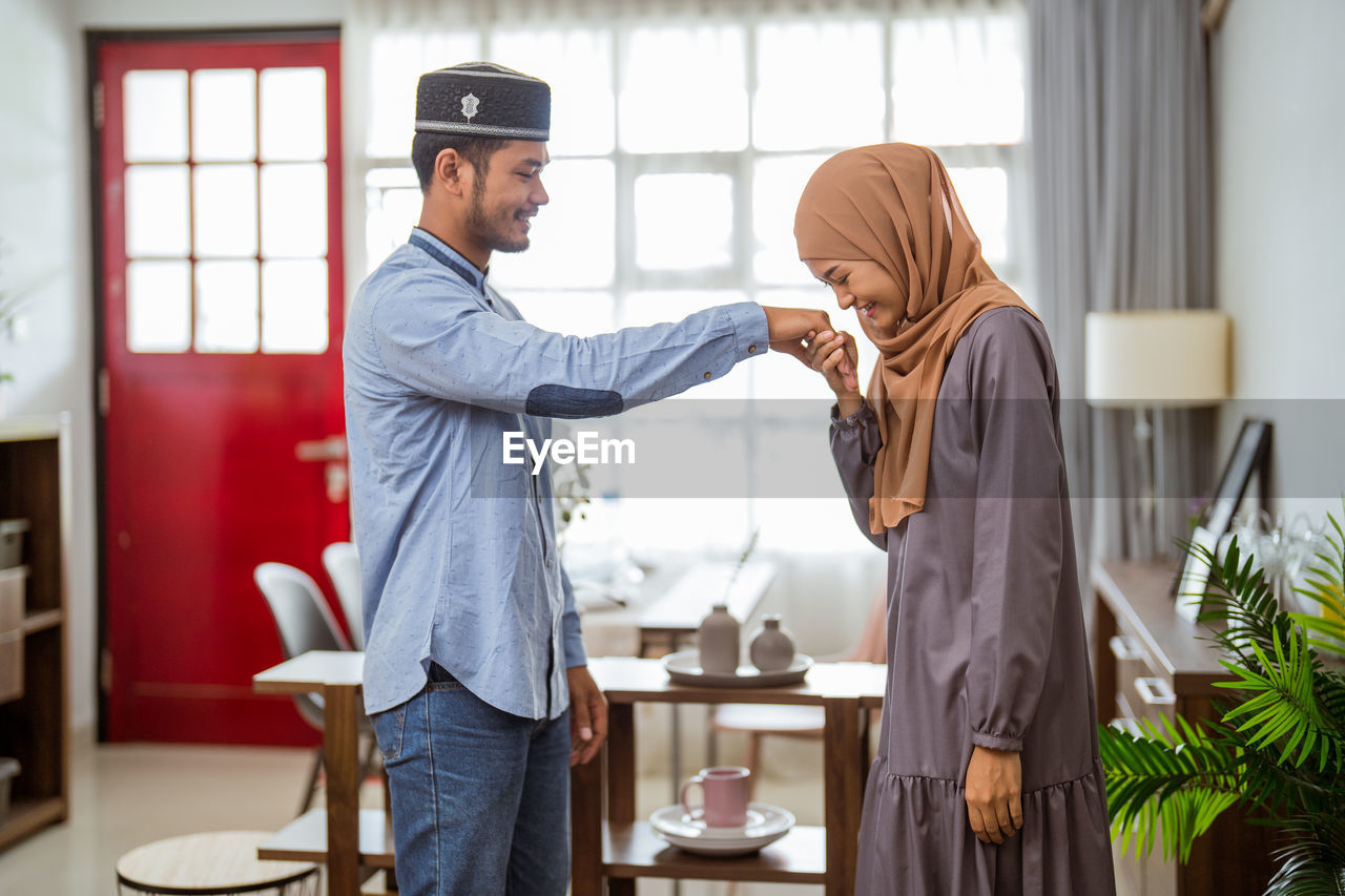 Smiling woman holding husbands hand at home