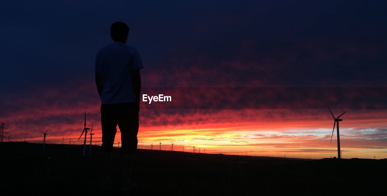 Rear view of man standing on field against cloudy sky at sunset