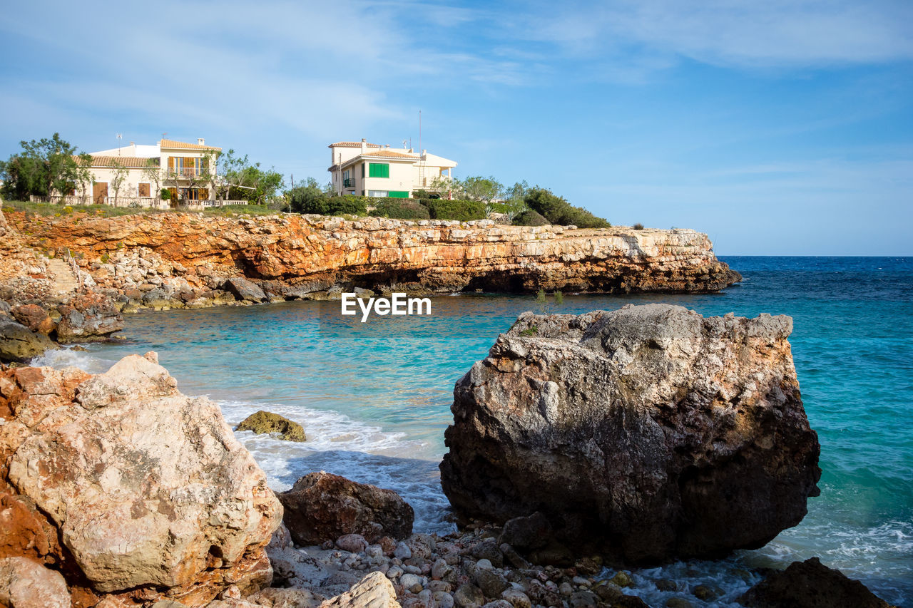 SCENIC VIEW OF SEA BY ROCKS AND BUILDINGS AGAINST SKY