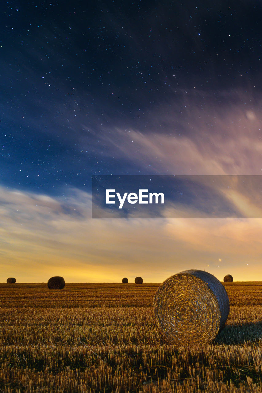 Hay bales on field against sky during sunset