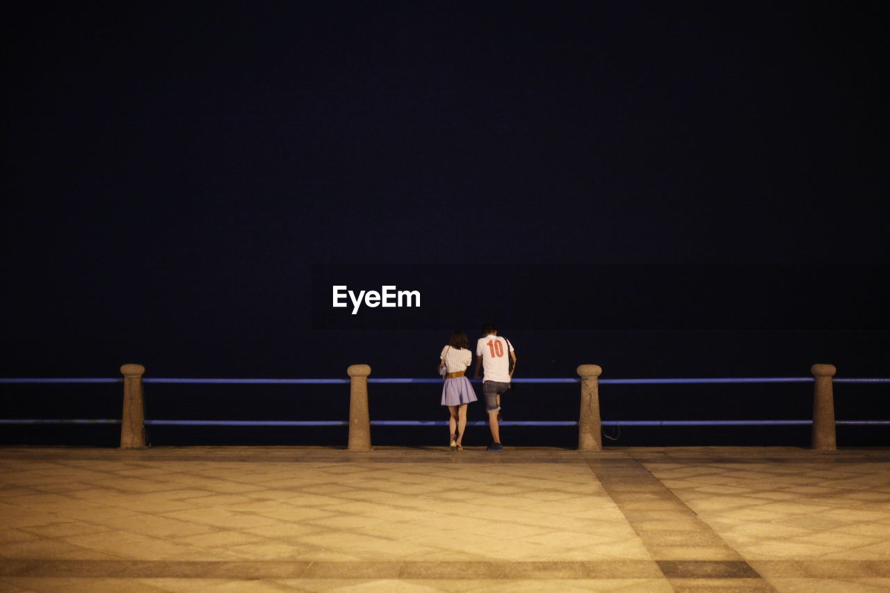 Rear view of couple standing by railing on promenade at night